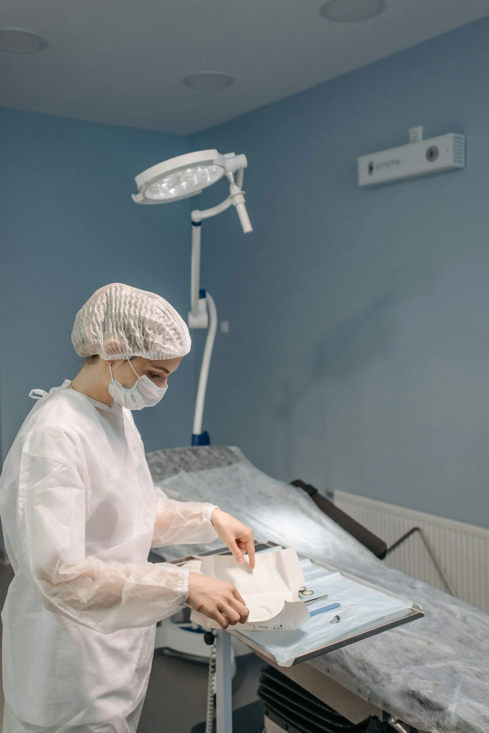 A healthcare worker in PPE preparing medical instruments in a clinical setting.